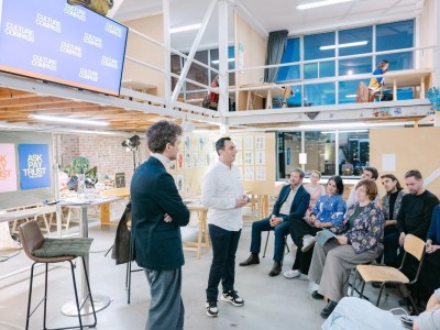 Two men standing, speaking in front of a small audience, indoors